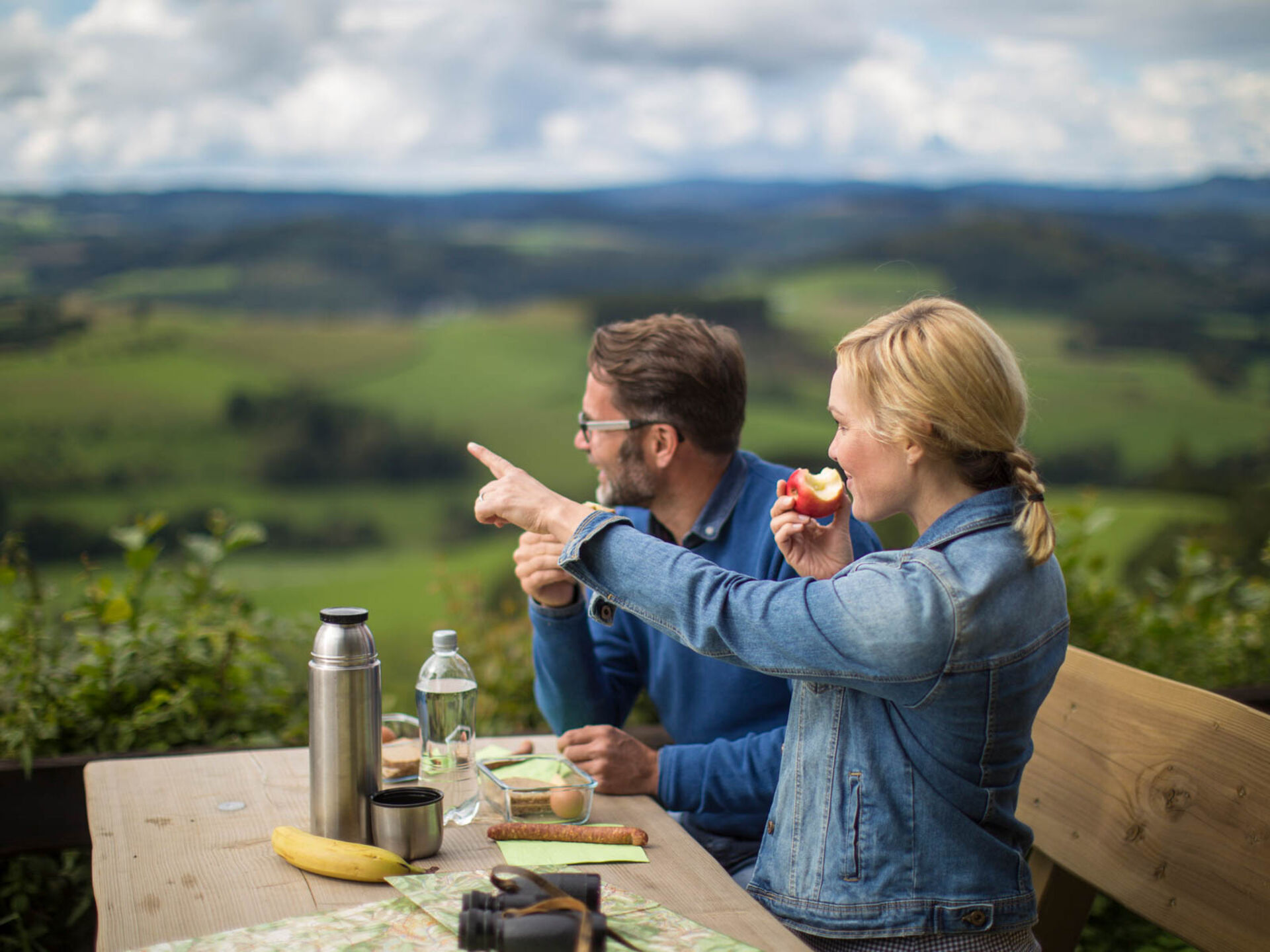 Ein junges Paar beim Picknick an einer Bank.